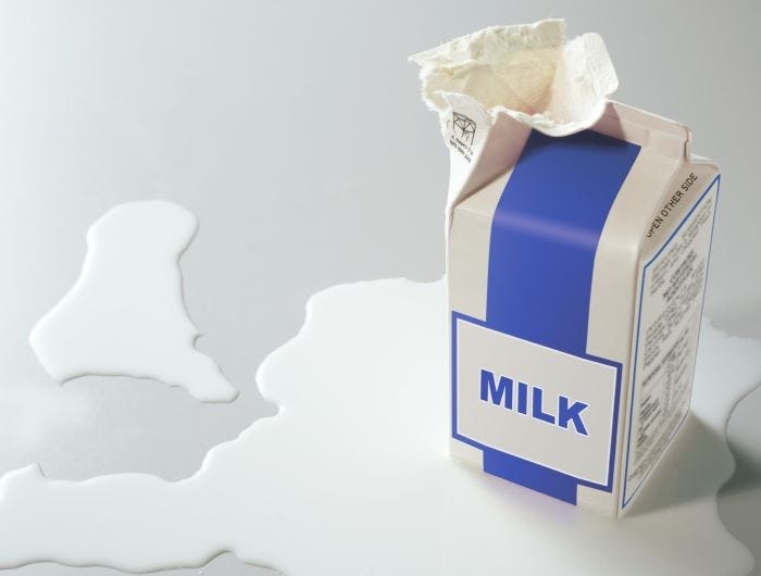 An opened paper milk carton in a pool of spilled milk