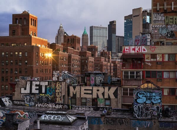 Buildings with a lot of graffiti on them in the foreground of a photograph that looks south from Manhattan’s Chinatown. No people are visible. 