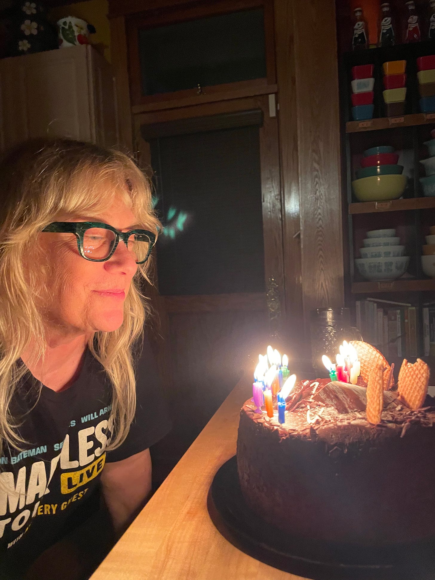 Susie Tweedy leans into a birthday cake with lit candles on it.
