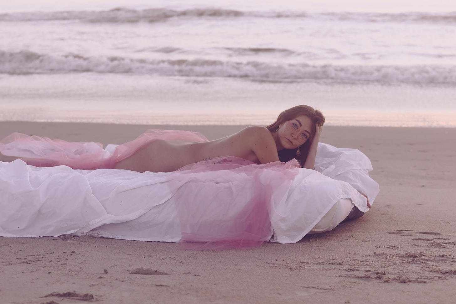 a naked woman lying on the bed at the beach sand
