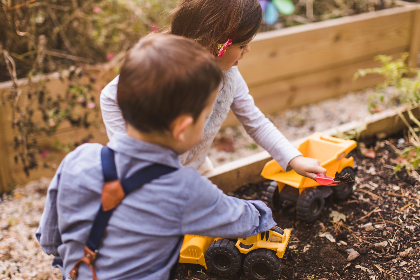 Kids playing with trucks in their garden beds.