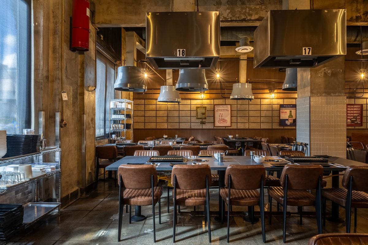 Leather backed chairs and tightly packed Korean barbecue grills on tabletops with steel hoods.