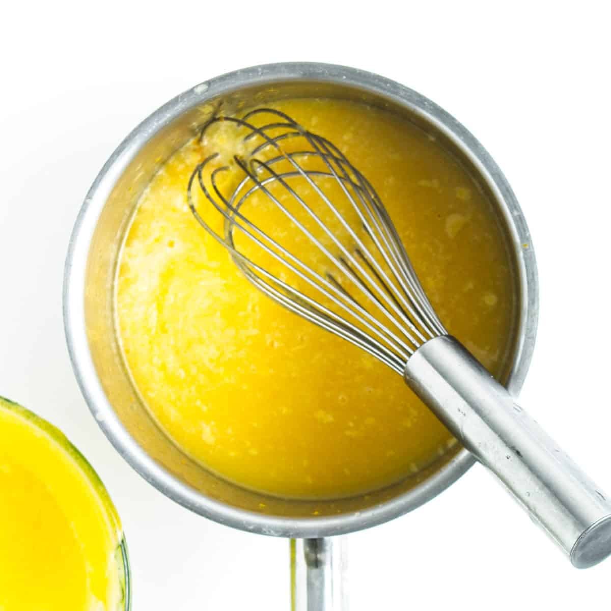 Saucepan with orange curd mixture and whisk.