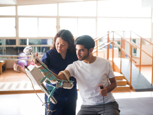 Male patient putting arm in device in physical therapist An athletic male patient putting his arm in a device for phyiscal therapy. rehabilitation technologies stock pictures, royalty-free photos & images