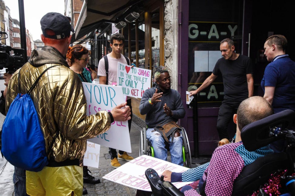 A group of disabled protesters hold signs and talk with bar staff outside a gay bar in London.