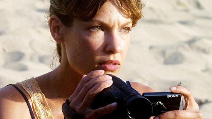 Movie still from The Perfect Getaway. A woman sits on a beach holding a video camera, looking concerned