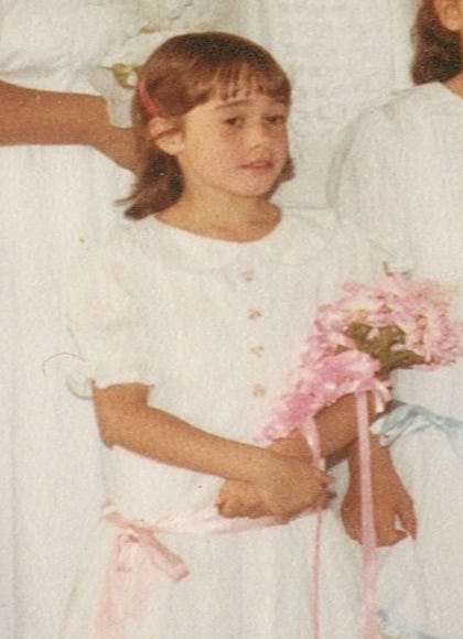 A young girl dressed in white holding a pink bouquet of flowers. 