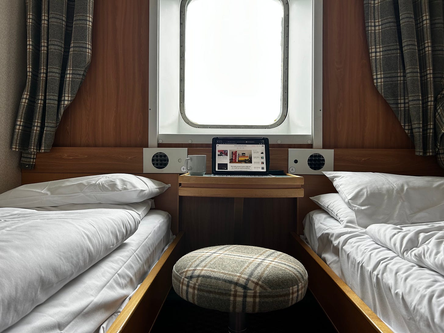 An iPad and coffee cup sit between two single beds in a cabin onboard a ferry.