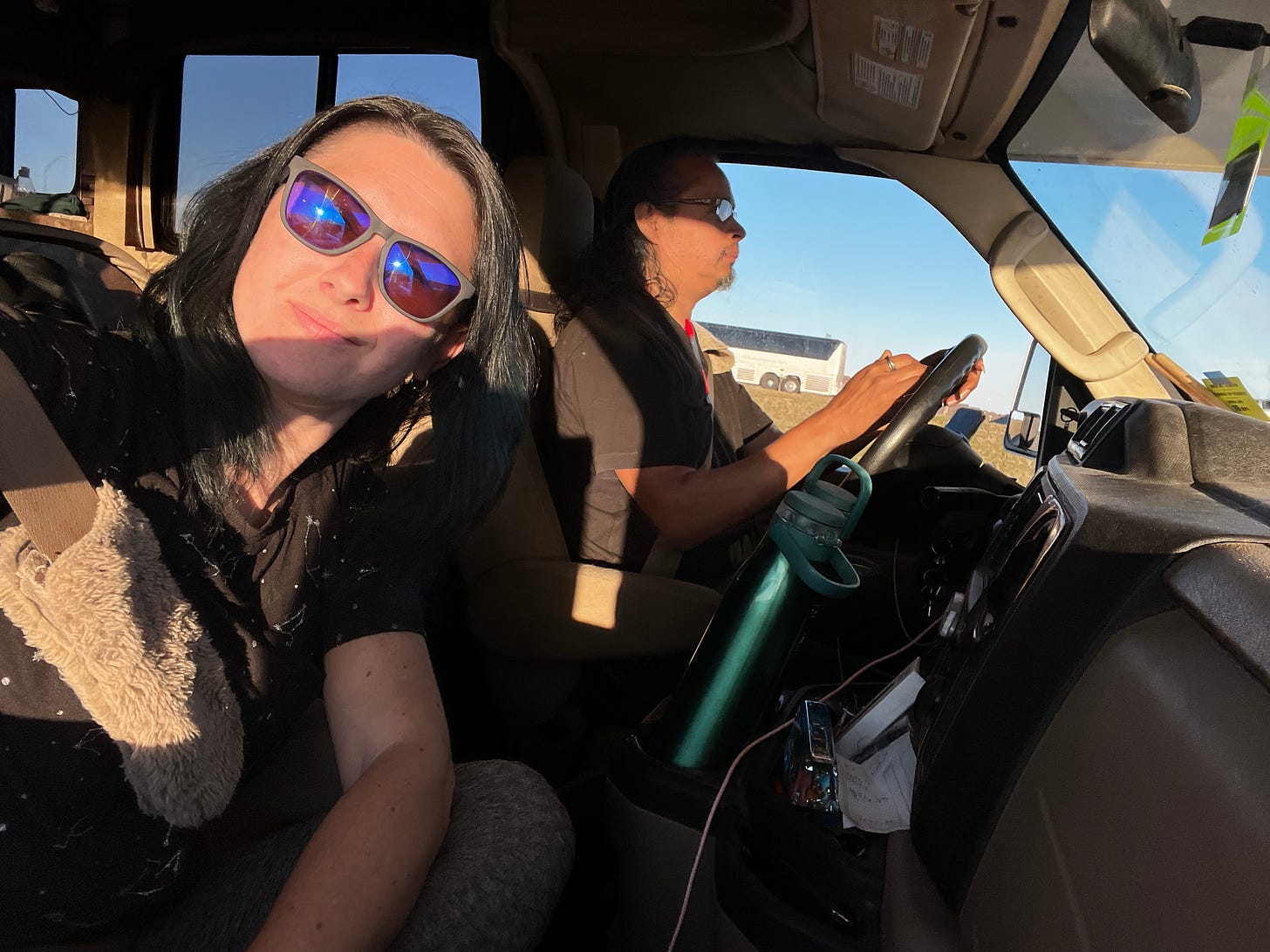 David driving the RV and Lyric in the passanger side. The sun leaves harsh shadows on both of them and Lyric is wearing sunglasses.
