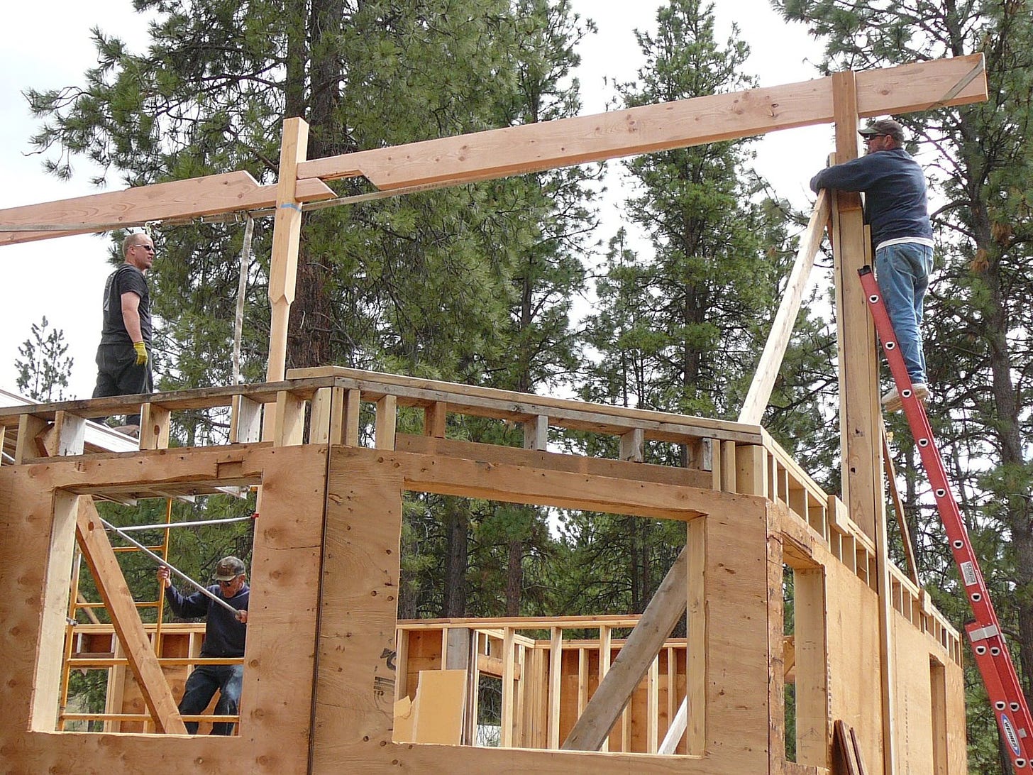 construction scene with one man on a ladder, another on a second story perch, and another on a scaffolding