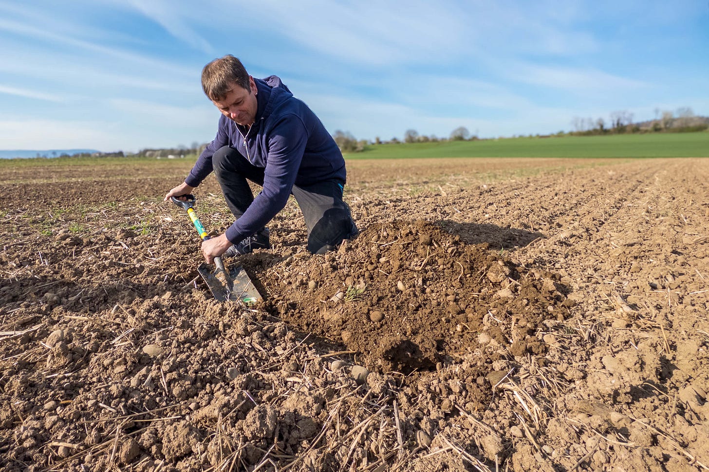 Gerhard Weisshäupl kniet auf einem Acker und entnimmt mit einem Spaten eine Bodenprobe. Die Szene zeigt ihn bei der Analyse der Bodenstruktur – eine zentrale Praxis der regenerativen Landwirtschaft zur Beurteilung der Bodenfruchtbarkeit. Gerhard Weisshäupl kniet auf einem Acker und entnimmt mit einem Spaten eine Bodenprobe. Die Szene zeigt ihn bei der Analyse der Bodenstruktur – eine zentrale Praxis der regenerativen Landwirtschaft zur Beurteilung der Bodenfruchtbarkeit.