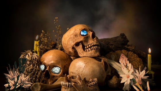 Flowers and candles adorn a pile of skulls. Jewels have been placed into the empty eye sockets.