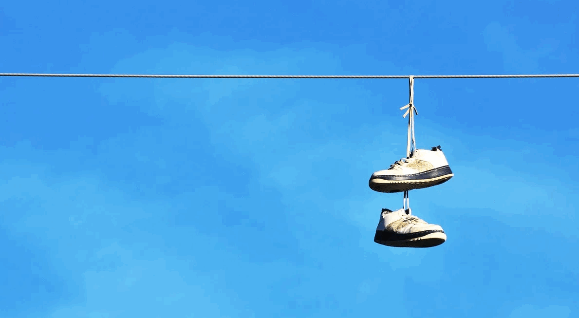 Sneakers hanging on a power line against a vast blue sky with wispy clouds.