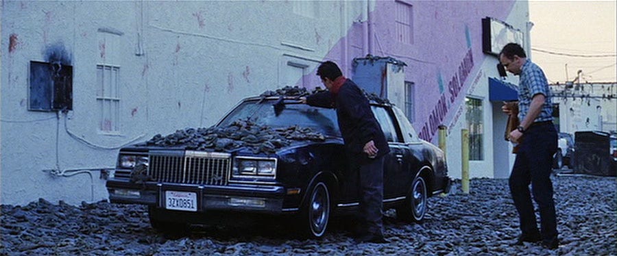 Shot from Magnolia of frogs covering the street and the top of a car. Two men look at the damage.