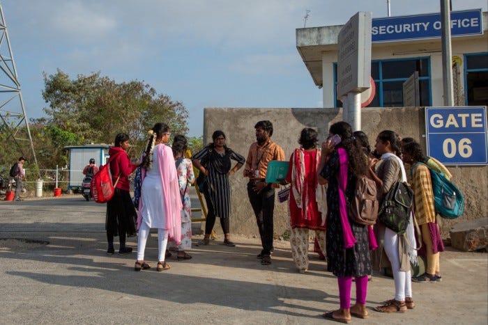 Job aspirants talk with a hiring agent outside a factory in India