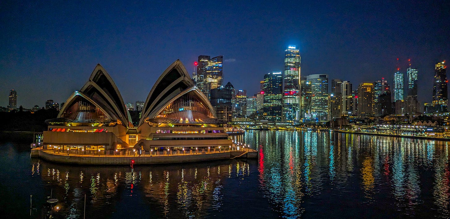 The Opera House glittering at night, downtown Sydney behind it. 