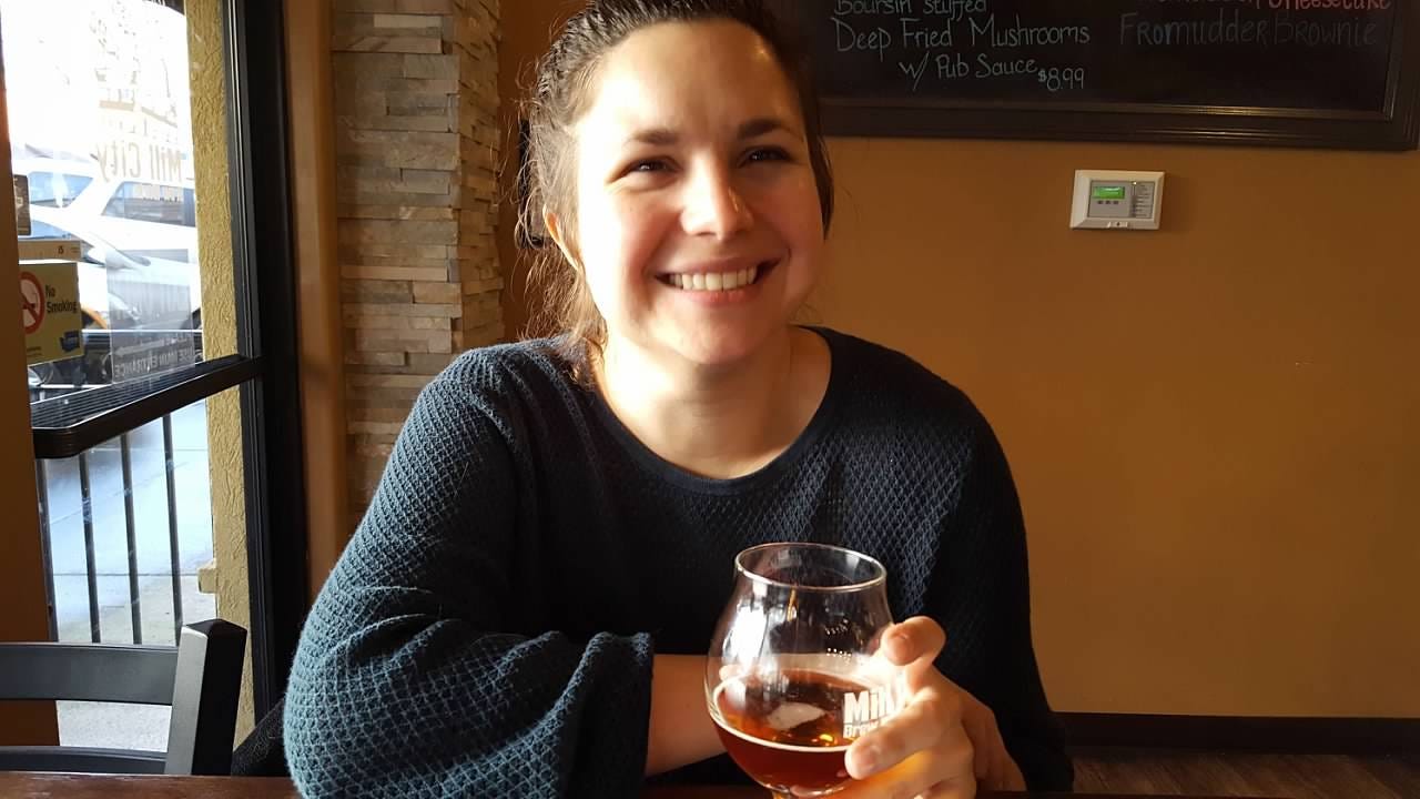 A brown-haired women laughs and sips a beer