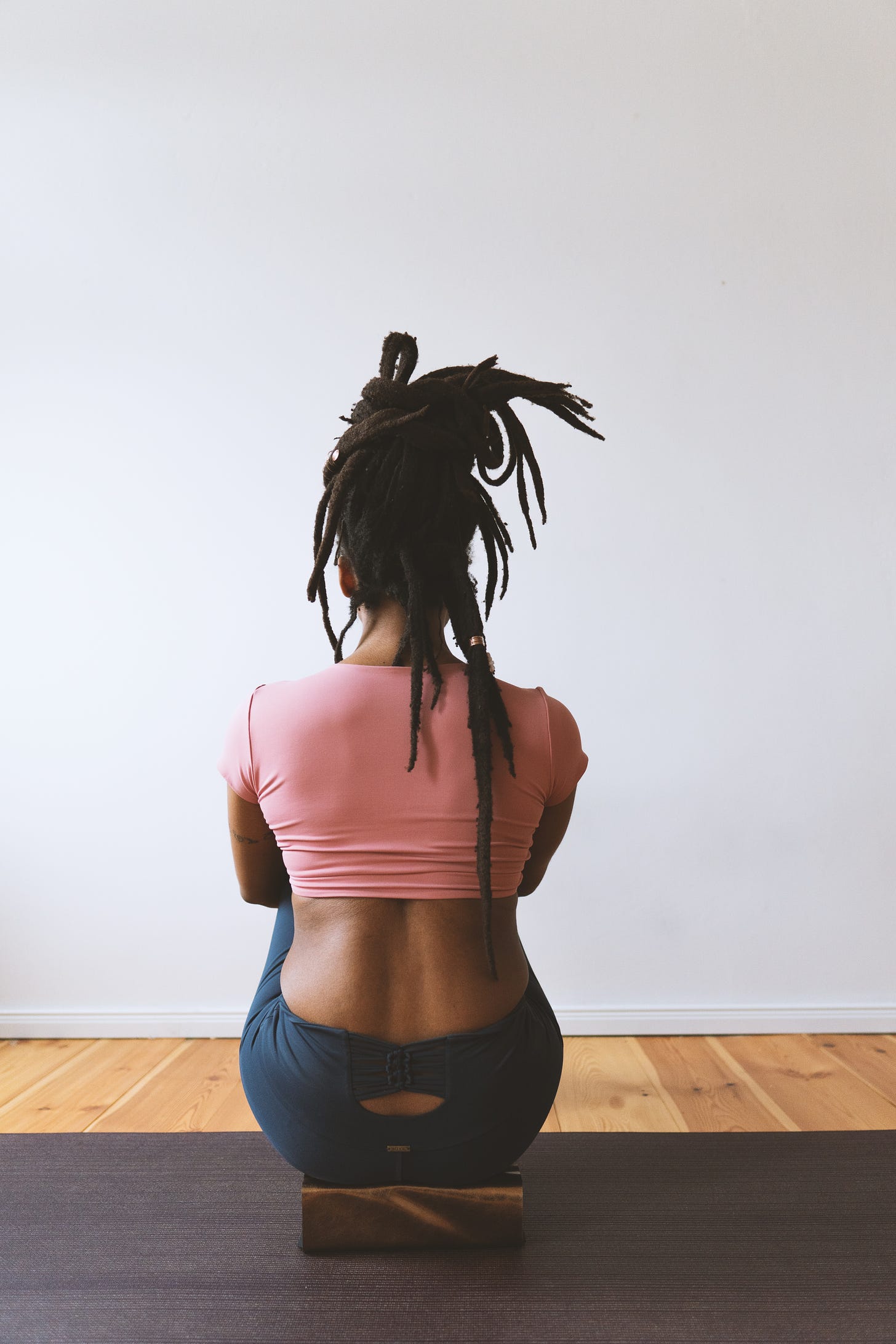 black woman with dreadlocks sitting on a yoga block with her back turned towards a wall