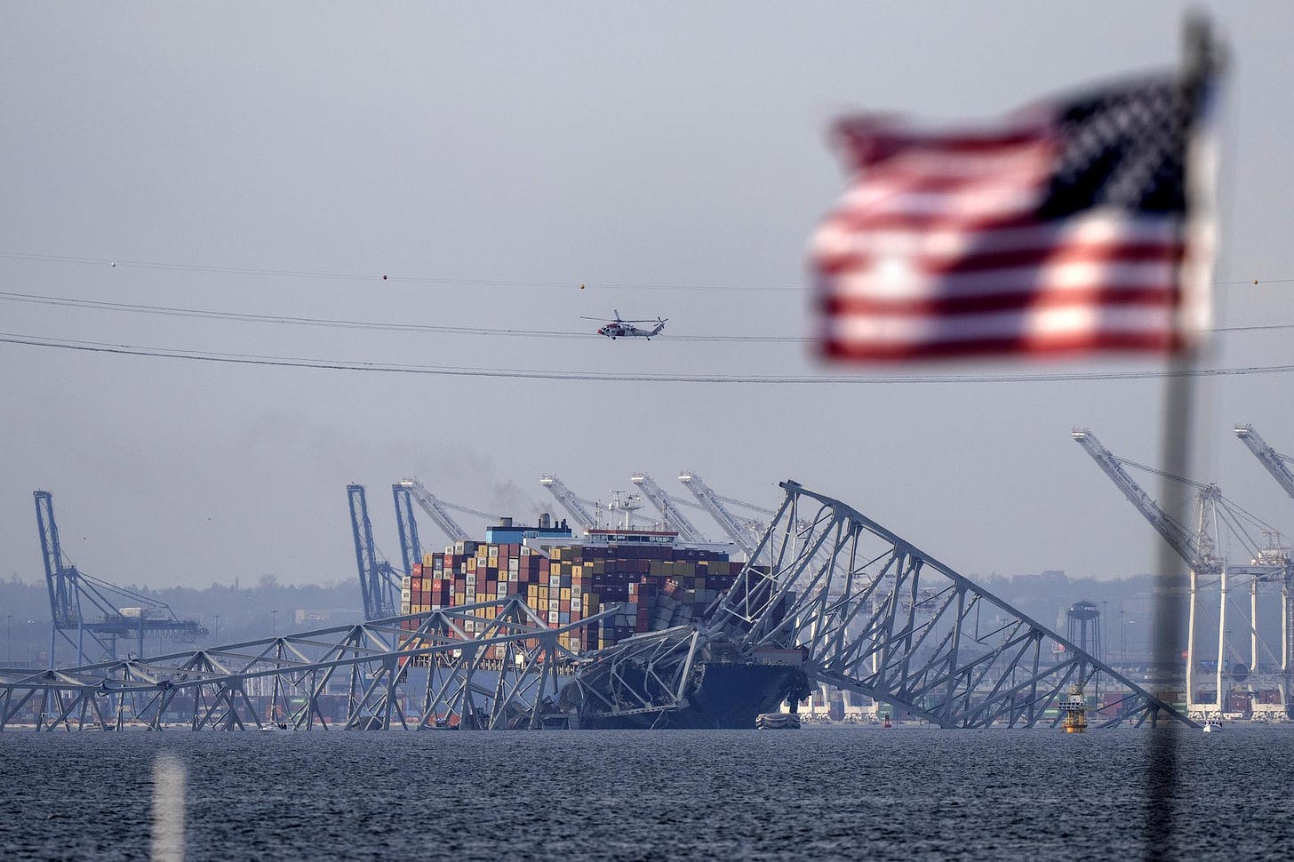An American flag flies on a moored boat near the container ship Dali and the wreckage of the Francis Scott Key Bridge.