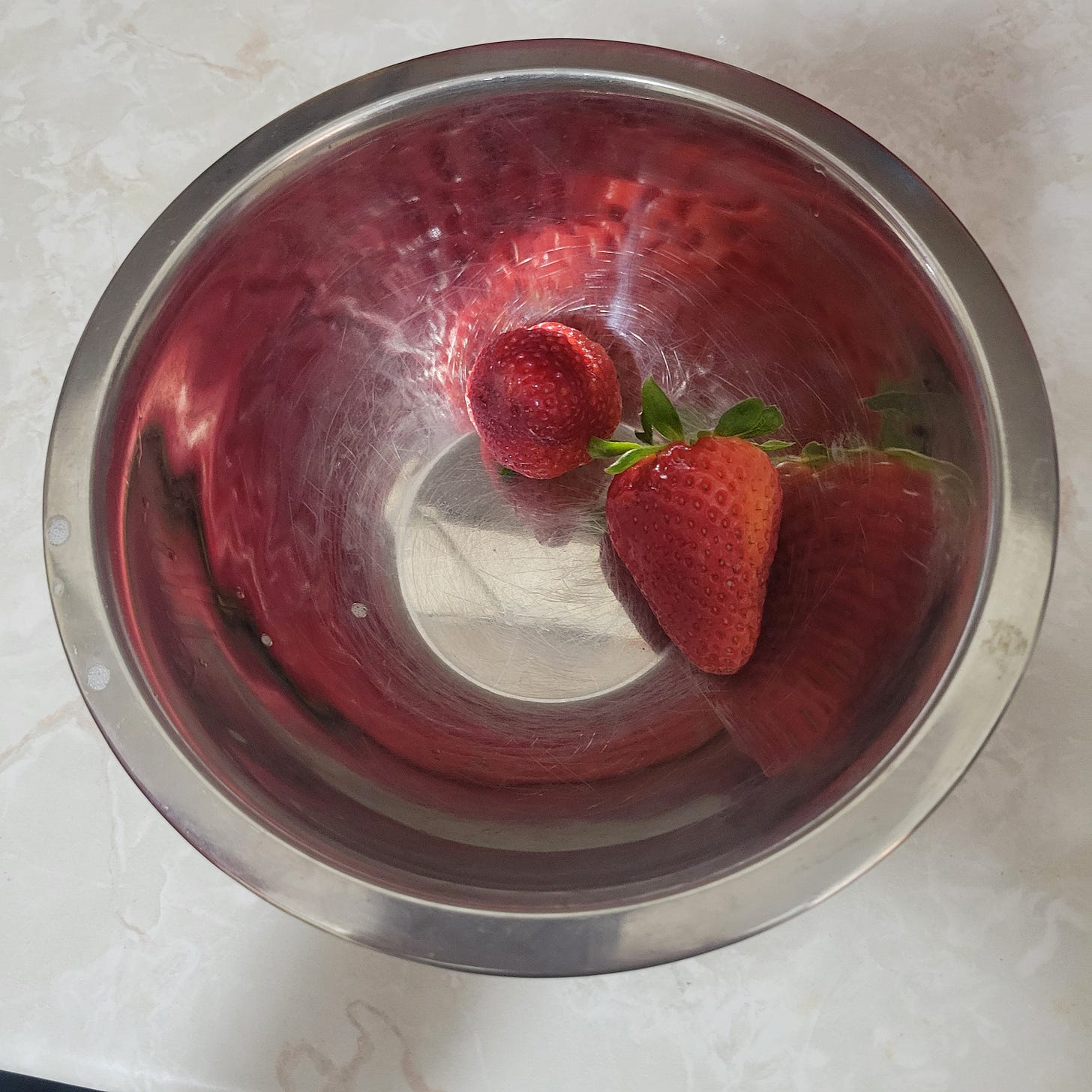 two strawberries in a metal bowl, reflecting light