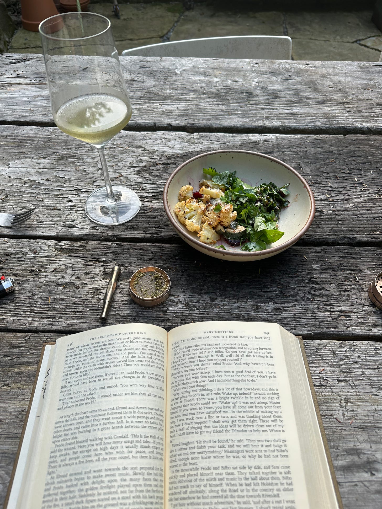 a glass of wine, a bowl full of vegetables, a one-hitter with weed, and Tolkien's Lord of the Rings opened up to the chapter called Many Meetings