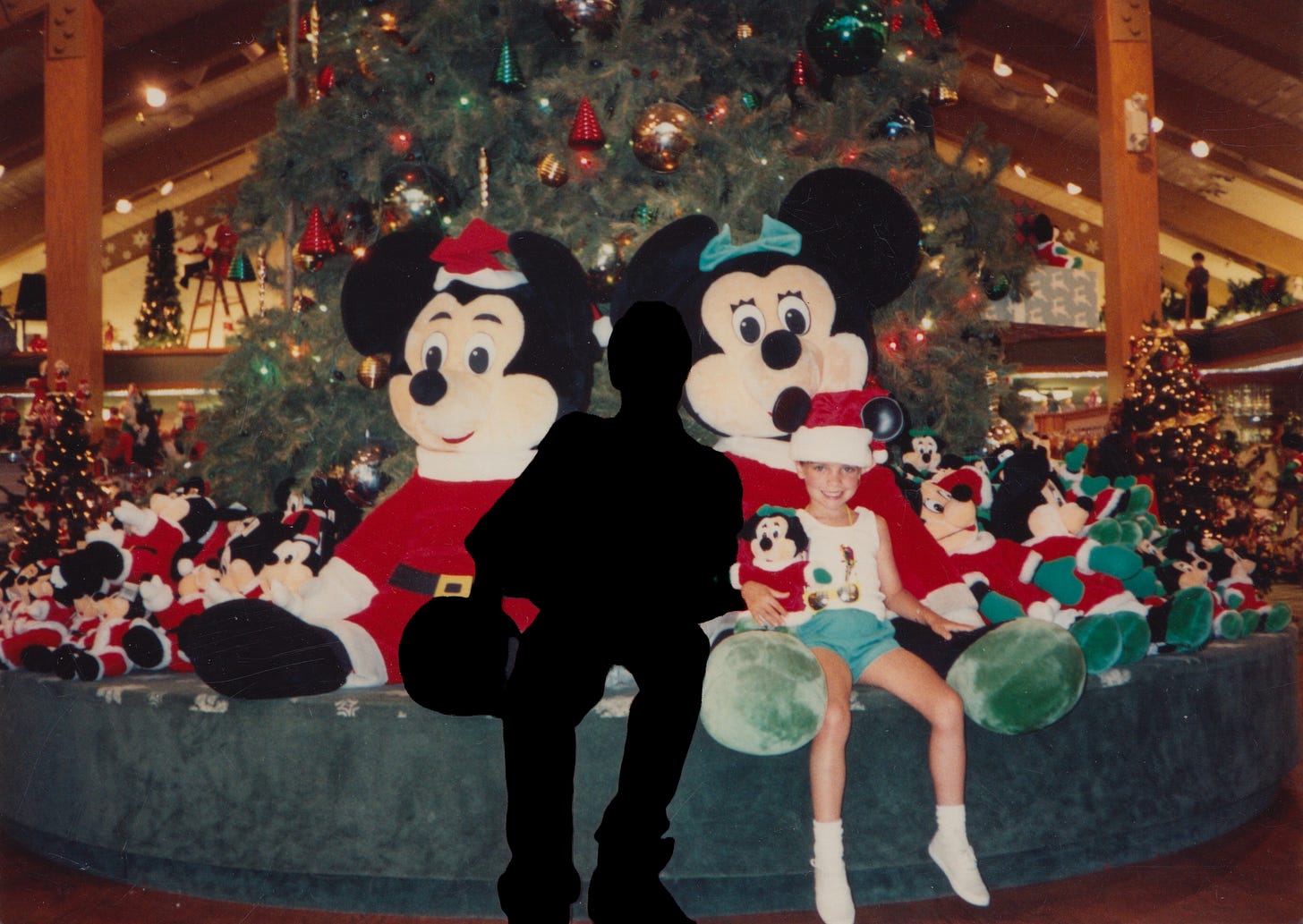 My brother and I sit on a Disney World display of stuffed Mickey and Minnie's during the holidays. He is silhouetted in black and I am around 8 years old.