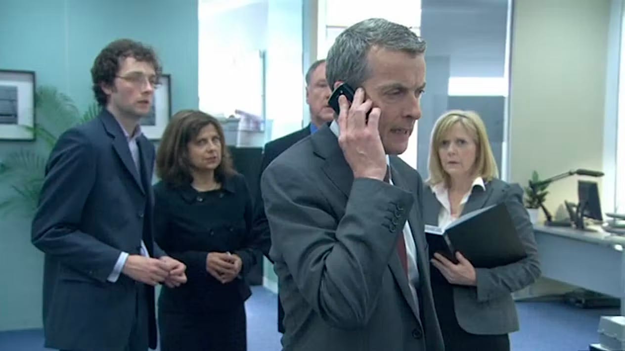 Still from The Thick of It - Malcolm Tucker on his cell phone in the office in front of a group of nervous subordinates.