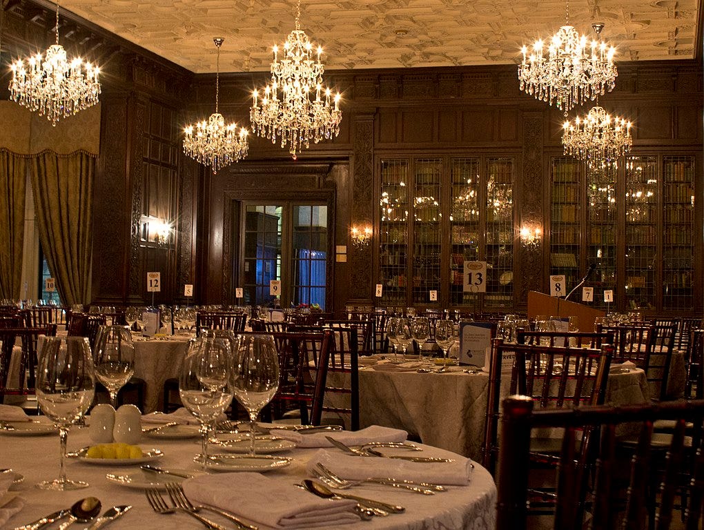 dimly lit room with crystal chandeliers hanging from the ceiling and brown wooden bookcases with glass fronts lining the walls