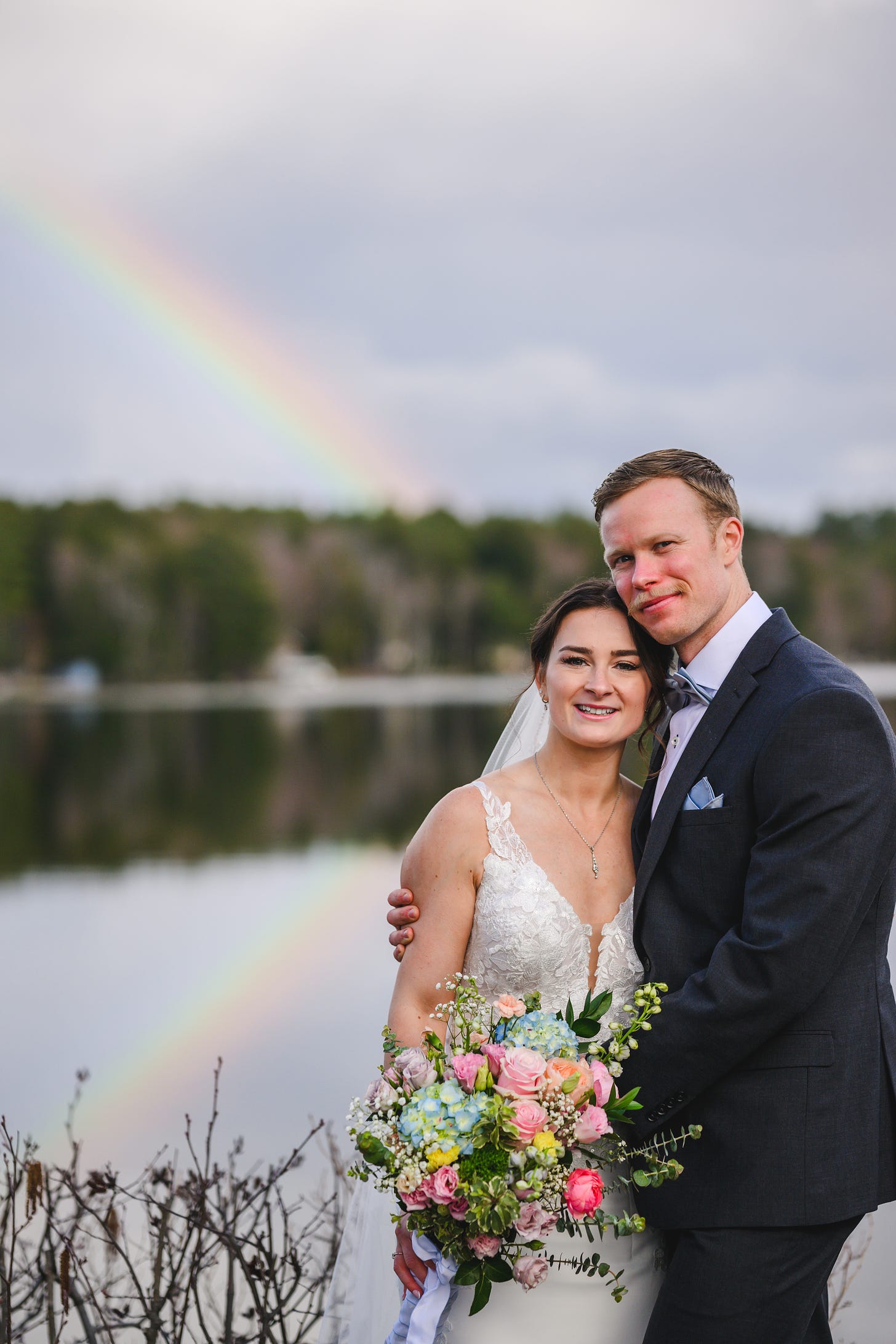 A bride and groom standing in front of a rainbow