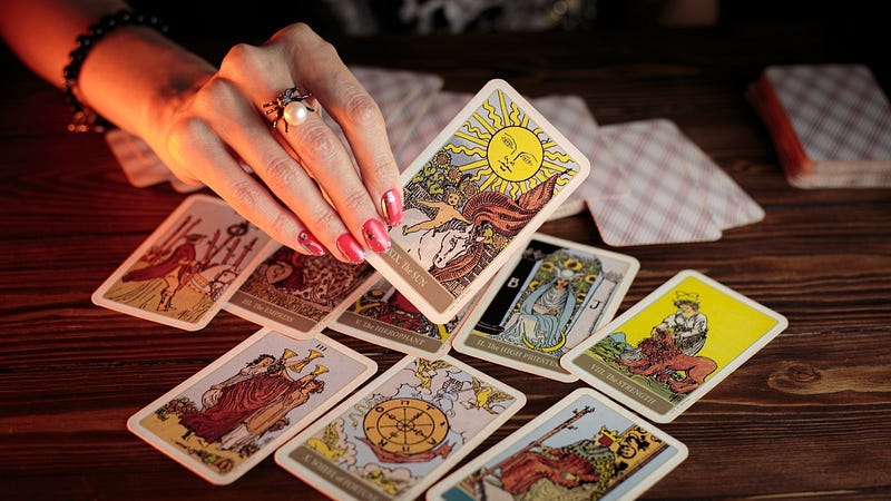 A hand holding a tarot card, above a table with assorted tarot cards placed on it.