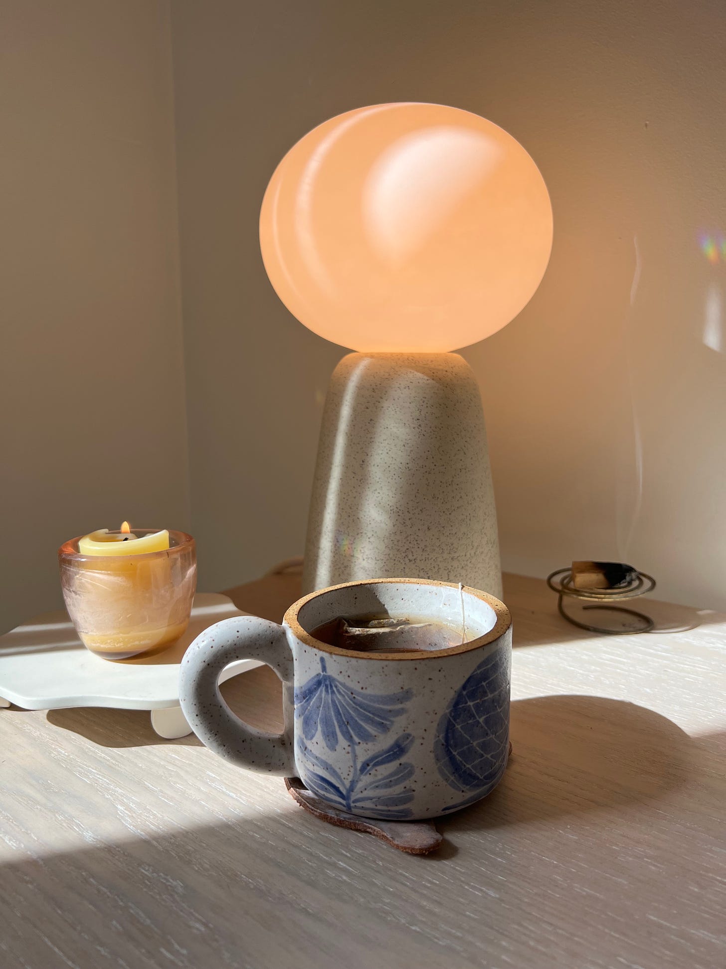Photo of a ceramic lamp, ceramic mug with blue illustrations, and a beeswax candle.