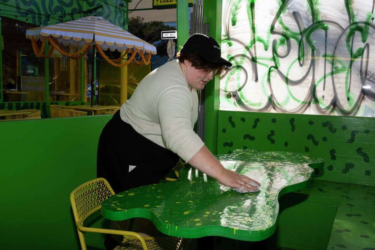 Camille Messerly wipes down a parklet table next to a window covered with graffiti at Shuggie’s in San Francisco on Tuesday, Sept. 26. The owners of Shuggie's have spent at least $3,000 to clean up frequent tagging of their parklet.
