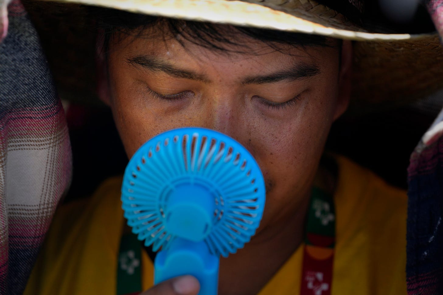 A World Youth Day volunteer uses a small fan to cool off from the intense heat, as he waits ahead of the Pope Francis arrival at Passeio Marítimo in Algés, just outside Lisbon, Aug. 6, 2023. 