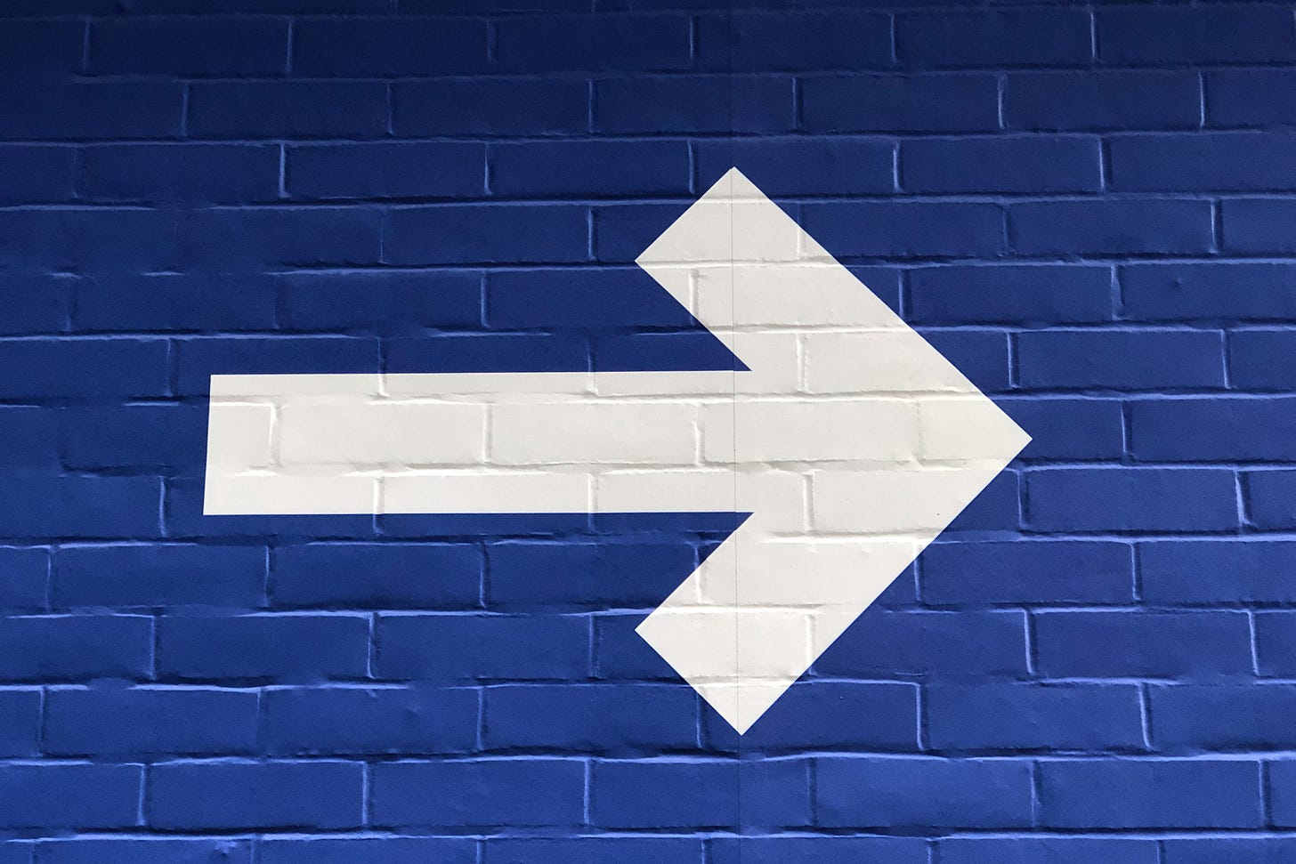 A white arrow pointing right, painted on a blue brick wall.