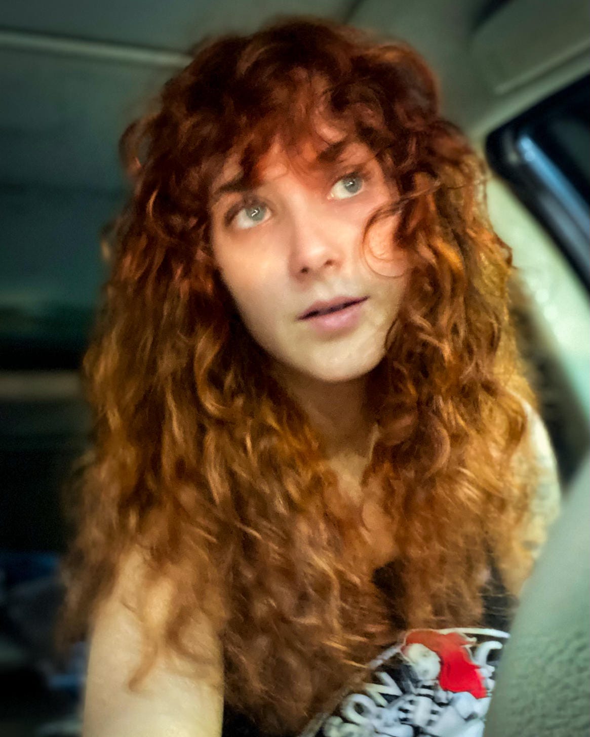 young woman with long curly red hair shown in soft focus looking to side