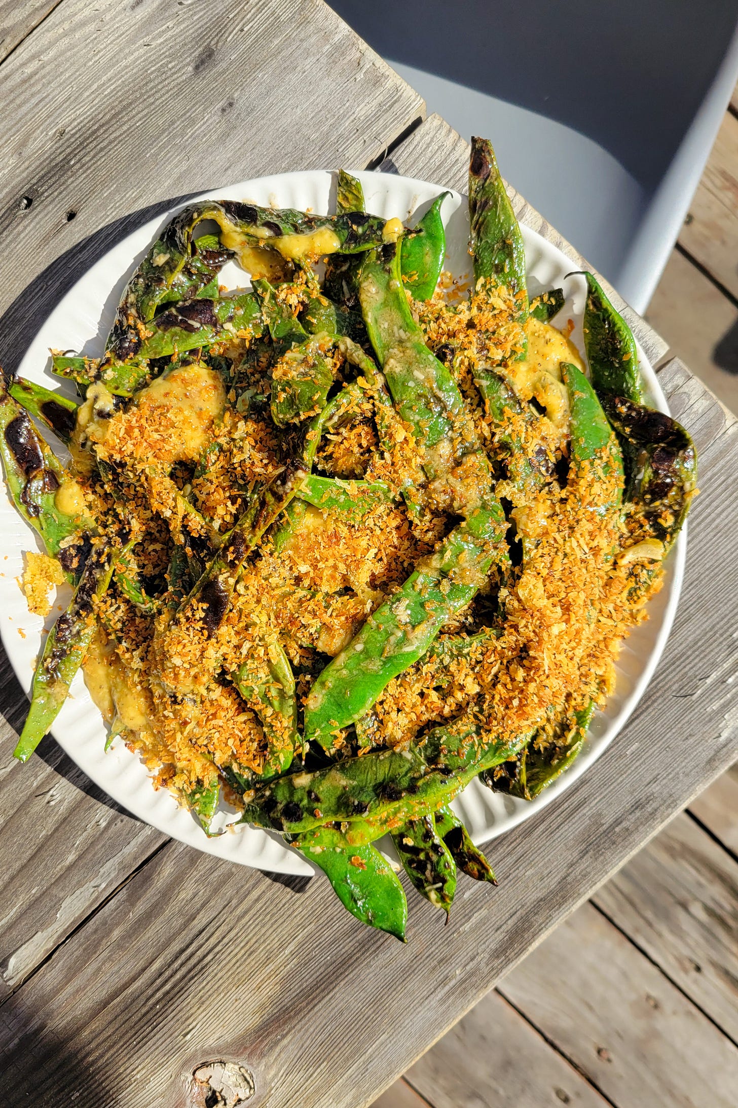 Plate of grilled green beans with caesar dressing and breadcrumbs on a wooden picnic table