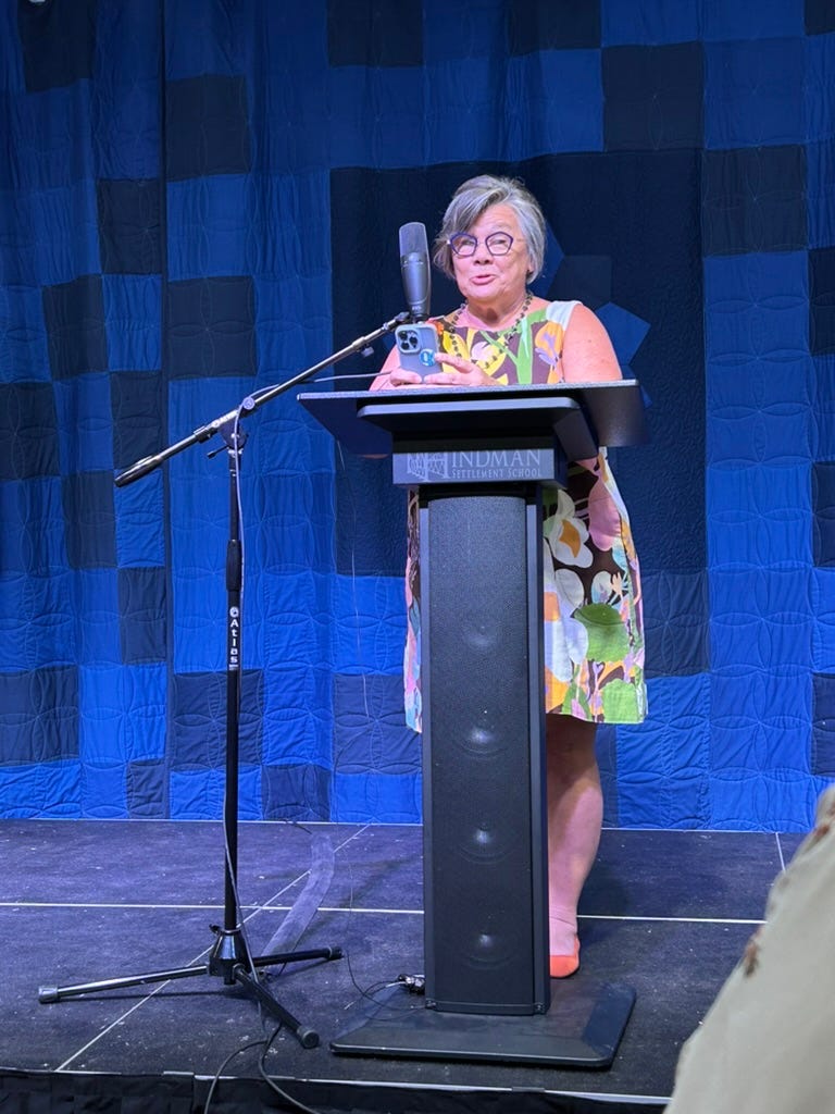 Woman in a flowery dress wearing glasses stands behind a microphone reading from her phone