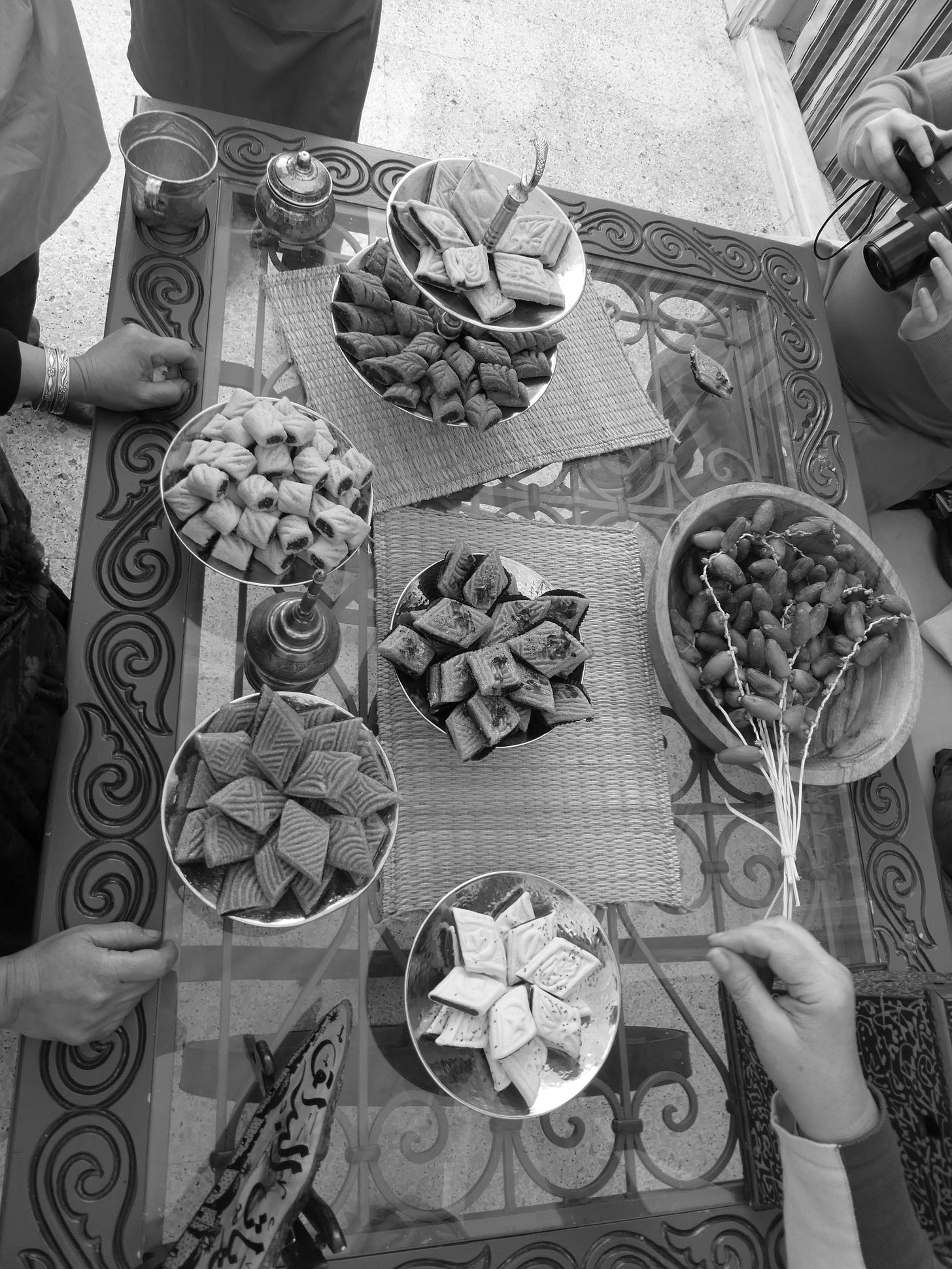 A rectangular table with different platters of various shaped and coloured makroudh