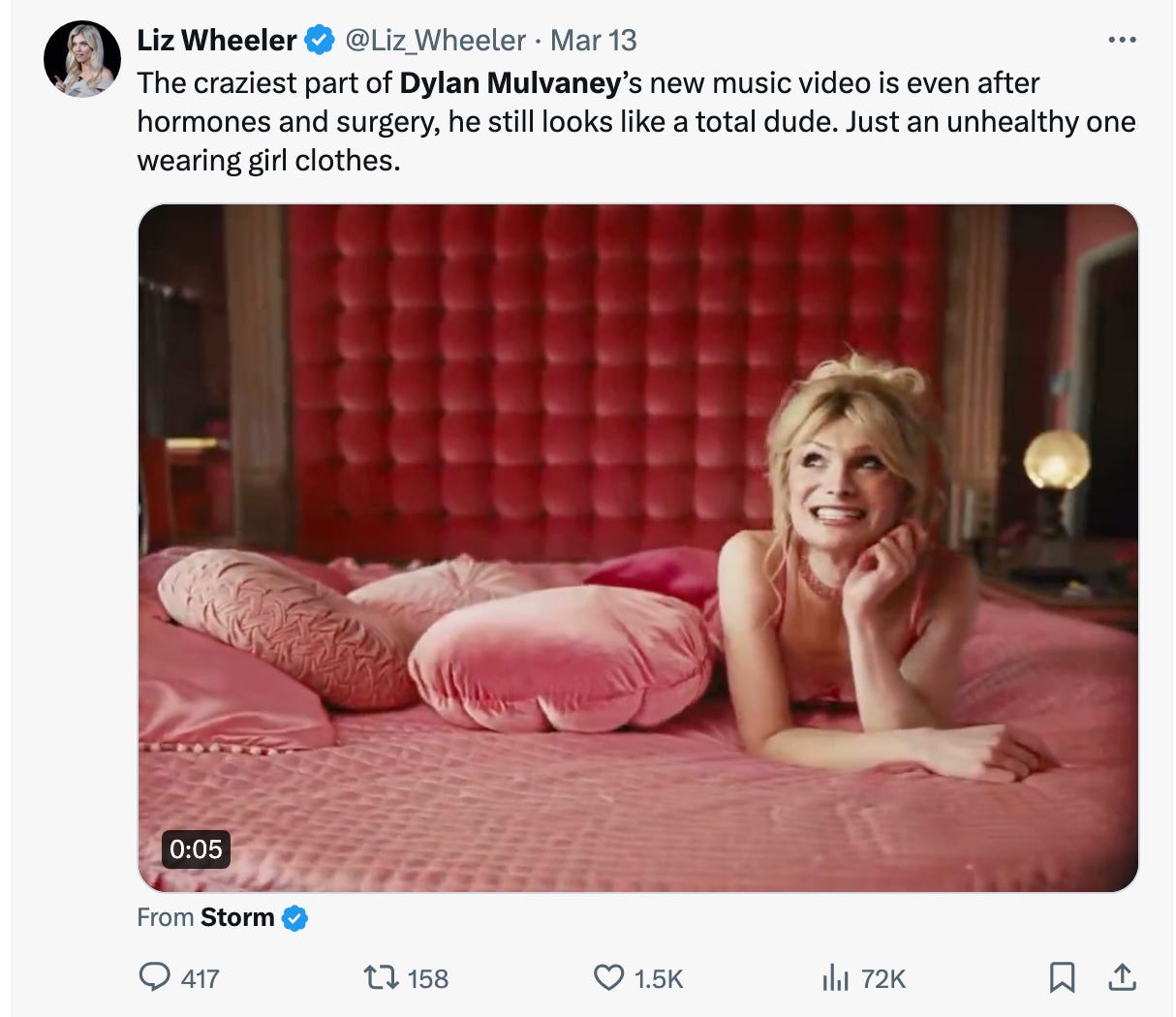 Dylan Mulvaney is smiling on a pink bed, under a hateful caption attacking her appearance.