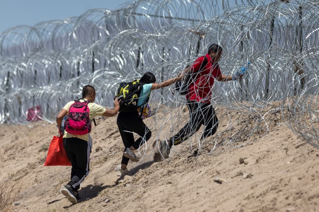 Immigrants walk through razor wire surrounding a makeshift migrant camp after crossing the border from Mexico on May 11, 2023 in El Paso, Texas.