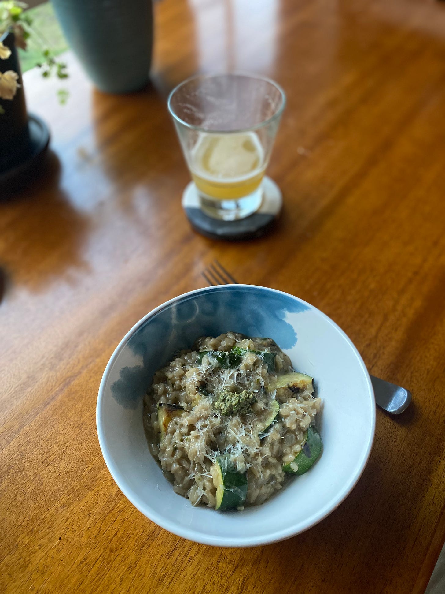 A blue and white bowl of pesto risotto with chunky half-moon pieces of grilled zucchini throughout. There's a dollop of pesto and some grated parmesan on top.