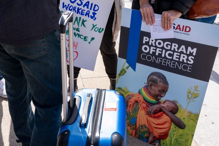 A laid off USAID employee holds a poster of her work, her oath of office, and a suitcase full of personal items, Friday, Feb. 28, 2025, after being given 15 minutes to clear out their items from USAID Headquarters in Washington. (AP Photo/Jacquelyn Martin)