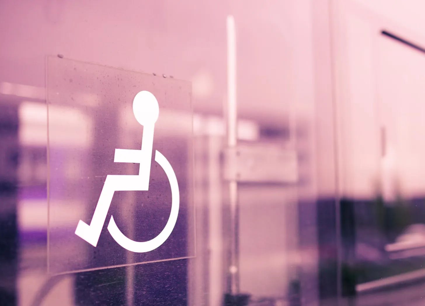 Wheelchair symbol decal on a pink tinted glass door