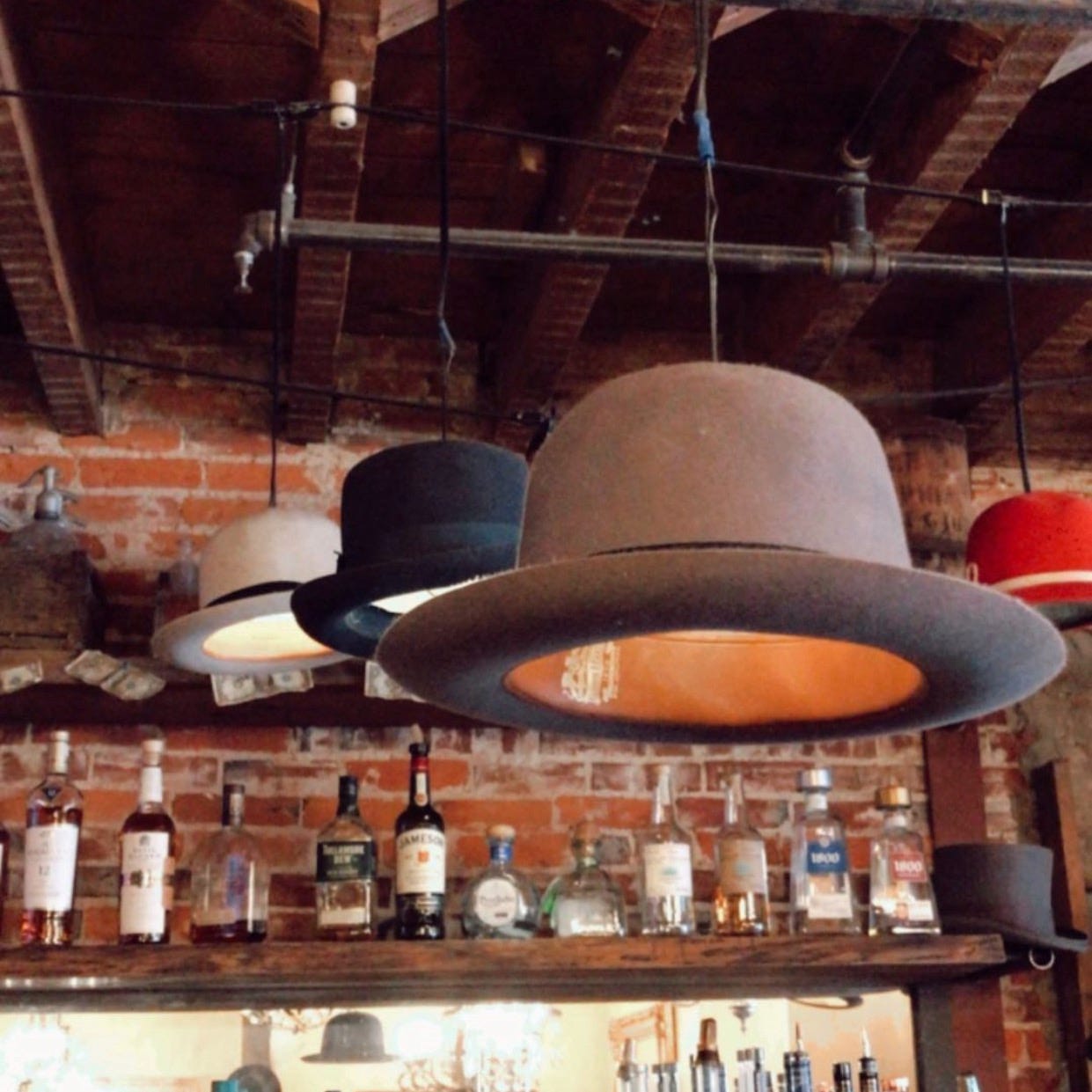 Three old bowler hats transformed into hanging lights, hang above a bar at a restaurant called the Hattery