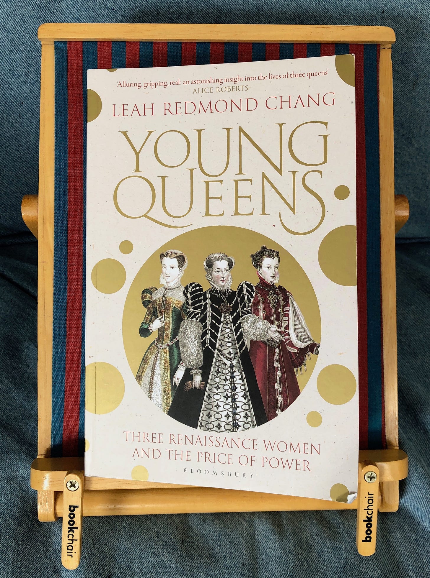 Leah Redmond Chang’s YOUNG QUEENS: THREE RENAISSANCE WOMEN AND THE PRICE OF POWER sits on a striped bookchair on a couch.