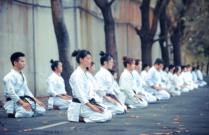 A row of people in karate uniforms sitting in meditation position