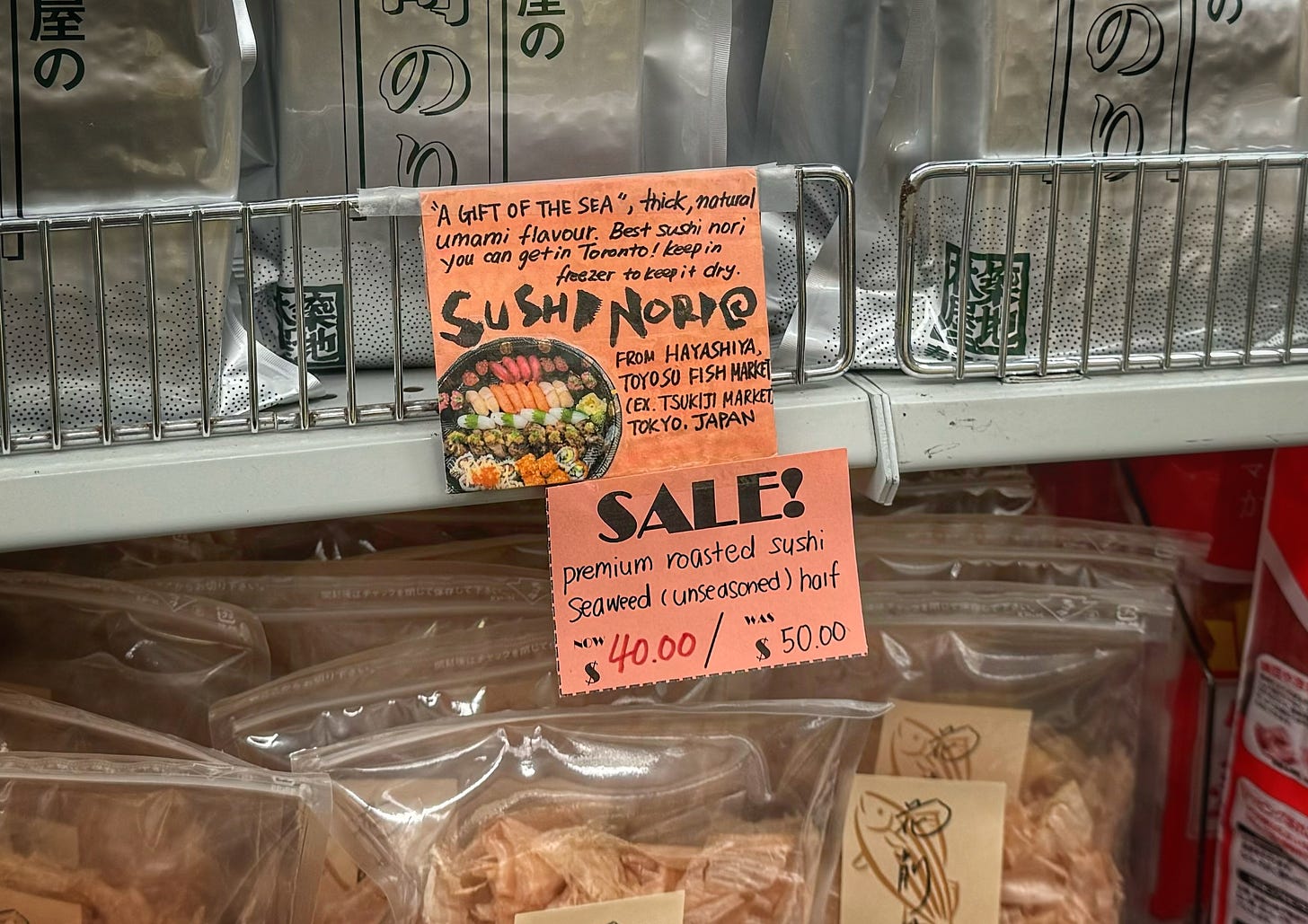 A handwritten sign attached to a shelf at Sanko reads, "Sushi Nori: "A gift from the sea" Thick, natural umami flavour. Best sushi nori you can get in Toronto! Keep in freezer to keep it dry. From Hayashiya Toyosu Fish Market (Ex. Tsukiji Market, Tokyo Japan." and "Sale! Premuim roasted sushi seaweed (unseasoned) half Now $40.00 Was $50.00"