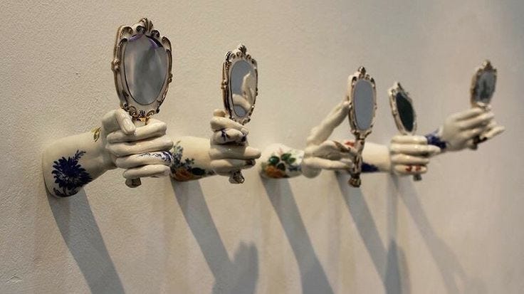 A row of porcelain hands mounted on a wall, each gripping a small ornate hand mirror. The hands are delicate, floral-patterned, and cast long shadows—reflecting nothing clearly back.