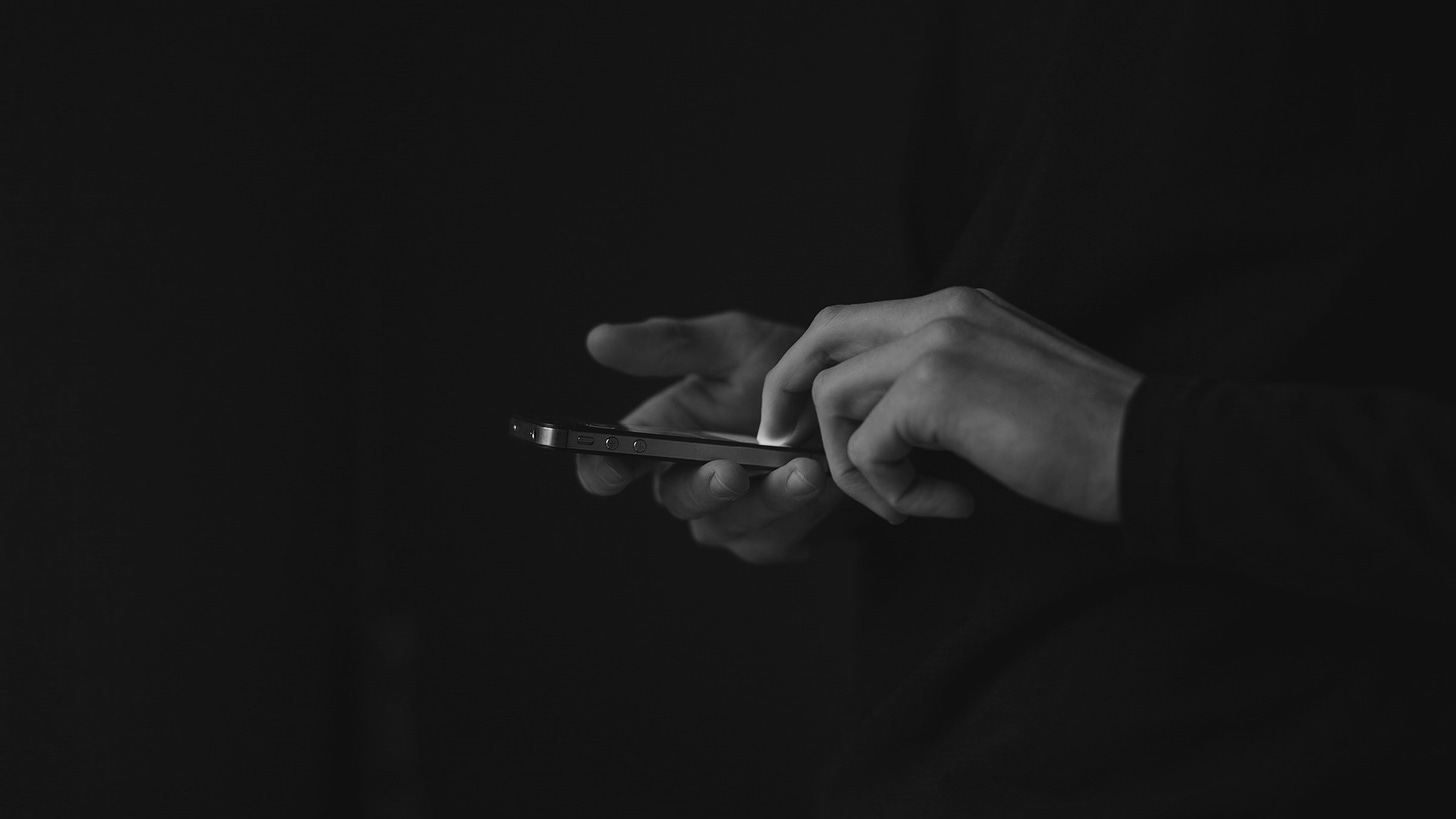 A pair of hands using a smartphone emerge from the darkness