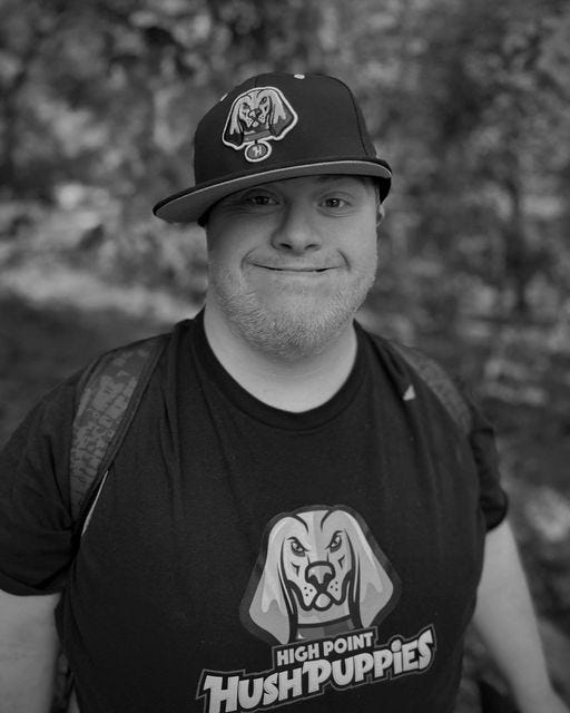 May be a black-and-white image of 1 person, beard, smiling, hat, park and text